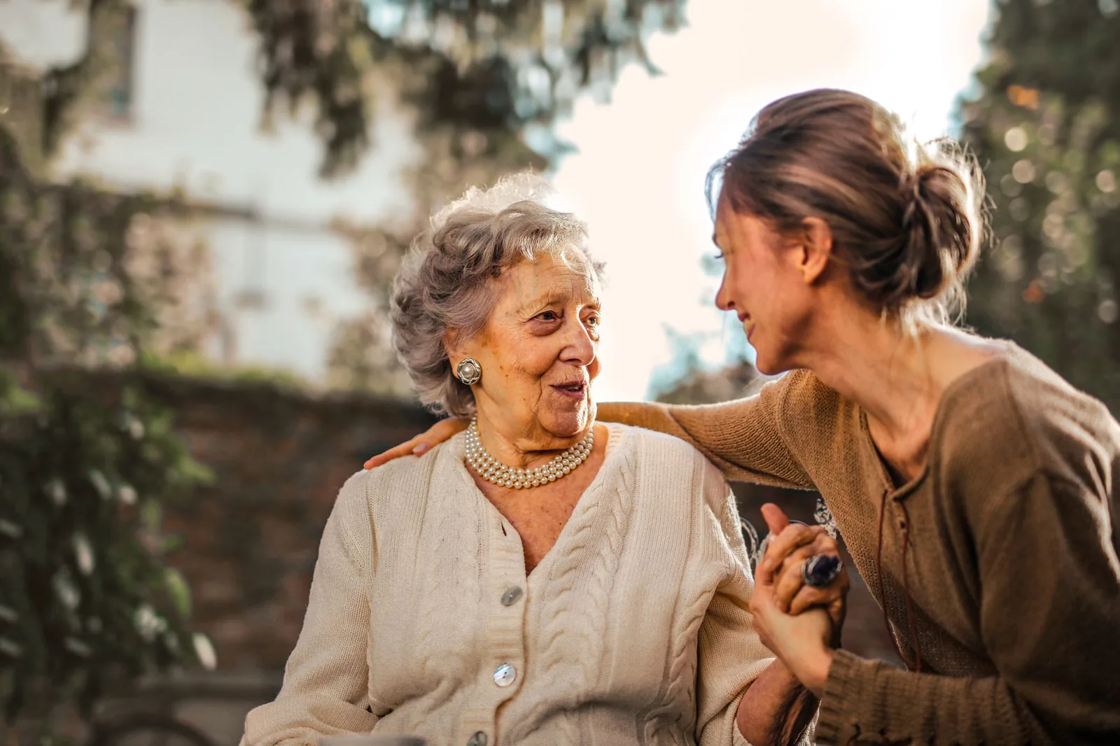 An older mother and her adult daughter sharing a happy moment in a garden